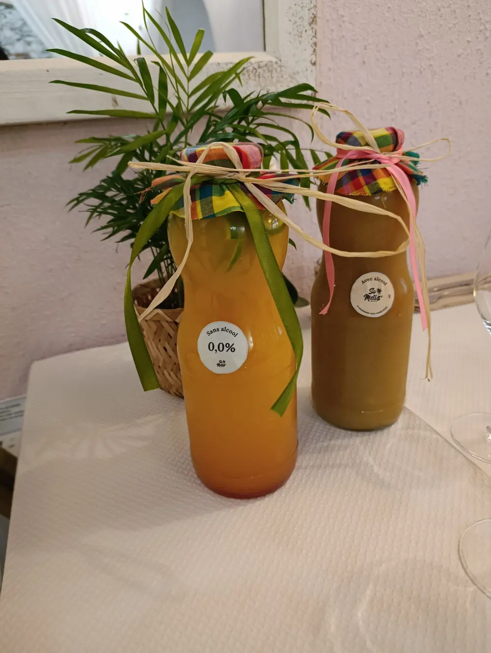 Deux bouteilles décorées de rubans sur une table, l'une contient un jus sans alcool, l'autre avec alcool.